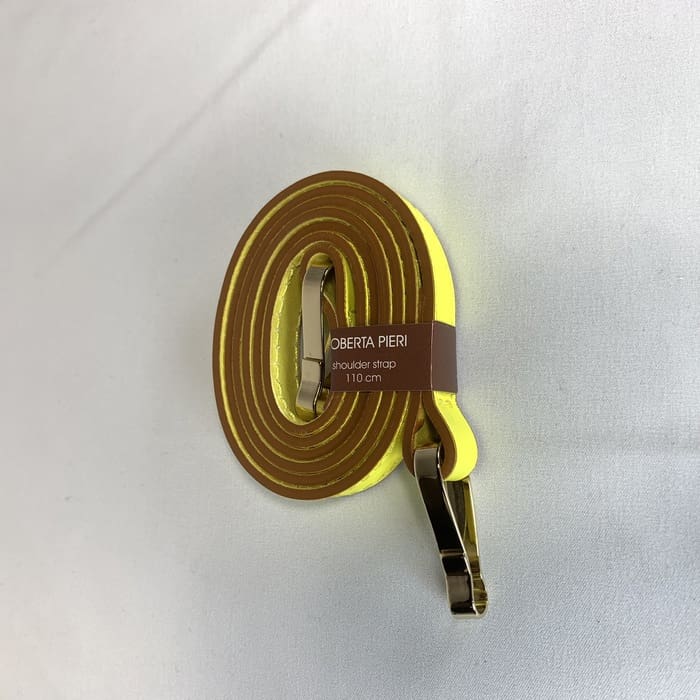 La tracolla gialla con finiture dorate è arrotolata e l'etichetta marrone "ROBERTA PIERI tracolla 110 cm" è adornata sulla superficie bianca.