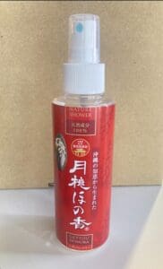 ベージュの背景に「Nature Shower」と書かれた赤いスプレーボトル。白いスプレーノズルとキャップ。.