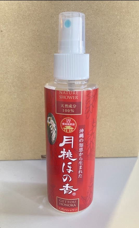 Un flacone spray rosso con la scritta "Nature Shower" su sfondo beige. Ugello e tappo di spruzzatura bianchi.